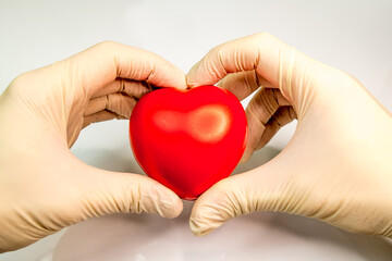 male hands in medical gloves holding a toy red heart