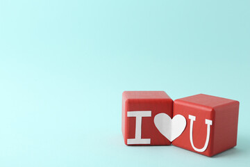 Phrase I Love You made of paper letters and heart connecting two red cubes on light blue background