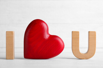 Phrase I Love You made of wooden letters and red heart on white table