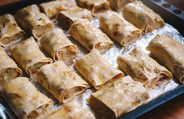 Lavash roll stuffed with potatoes, cabbage and herbs. Rolls on a baking sheet ready to bake. Selective focus.