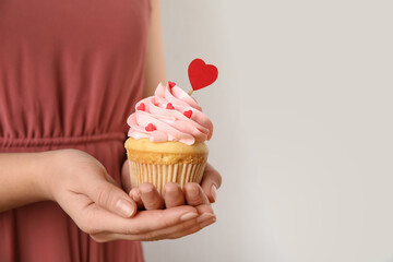 Closeup view of woman holding tasty cupcake on light background, space for text. Valentine's Day celebration