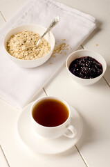 white cup of tea and a plate of oatmeal with currant jam on white background