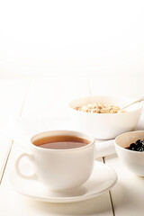 white cup of tea and a plate of oatmeal with currant jam on white background