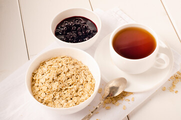 white cup of tea and a plate of oatmeal with currant jam on white background