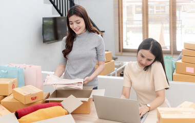Two beautiful Asian women are checking orders by laptops via the internet. And pack the paper box...