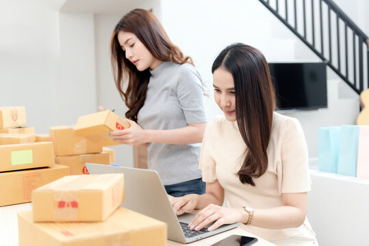 Two beautiful Asian women are checking orders by laptops via the internet. And pack the paper box With a happy smiling face, being a new normal online business