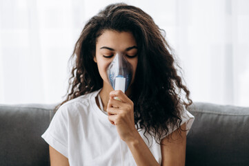 Close-up photo of sick african american woman with an inhaler. Unhealthy millennial girl doing inhalation at home, she use nebulizer and inhaler for the treatment. Cough and flu - obrazy, fototapety, plakaty