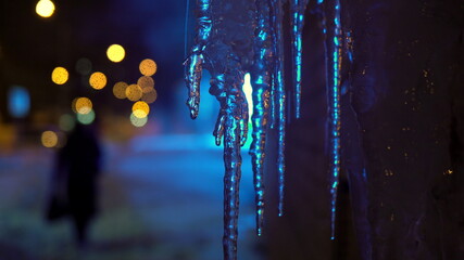Winter Russian evening. Icicles melt from warm air, neon light in the background