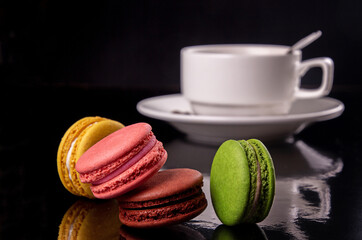 colorful macarons and cup of coffee over on black background.