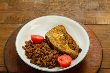 A plate of fish with lentils and tomatoes on a wooden table.