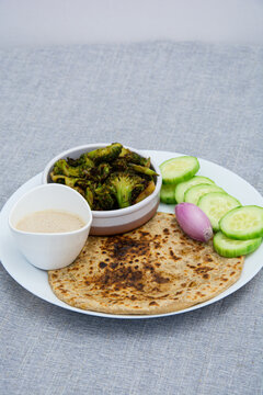 Aloo parotha in a white plate with onion, salad and broccoli fry with raita . An indian healthy breakfast