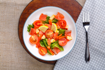 Salad with cold salmon and cherry tomatoes in a plate on a gray background on a wooden stand a stand next to a fork.