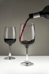 Red wine is poured from a bottle into a glass on a blurred background, close-up.