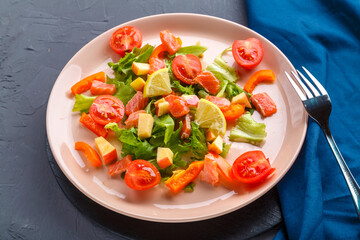 Salad with salmon and cherry tomatoes on a concrete background on a blue napkin next to a fork.