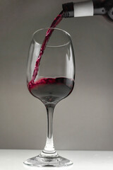 Red wine is poured from a bottle into a glass on a blurred background, close-up.