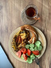 Traditional Turkish tea in tea glass and Turkish bagel, tomato slices, cucumber slices in the plate on a wooden table. daylight comes through the window
Turkish breakfast, alone 