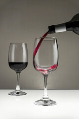 Red wine is poured from a bottle into a glass on a blurred background, close-up.