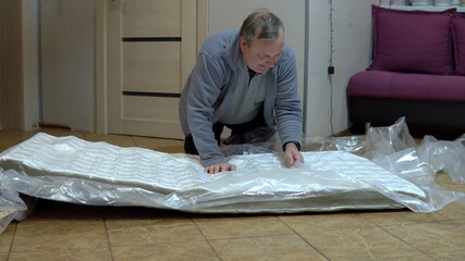 A grown man unpacks a new mattress. Unpacking the mattress with a knife pressed into the bag
