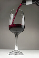 Red wine is poured from a bottle into a glass on a blurred background, close-up.