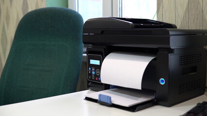 The printer on the table has printed a blank sheet. Office space, table, chair and printer