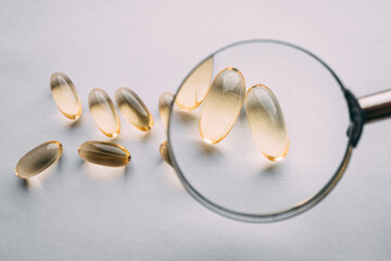 yellow transparent omega 3 capsules under a magnifying glass. vitamin development concept