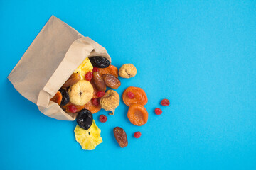 Top view of different dried fruits in a paper bag on the blue background
