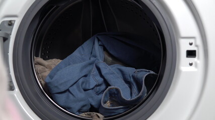 Girl loads dirty things into the washing machine close-up