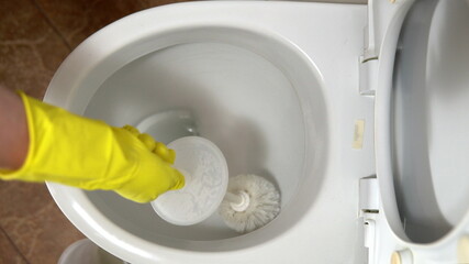 A housewife in rubber gloves cleans the toilet bowl with a special cleaner and a brush