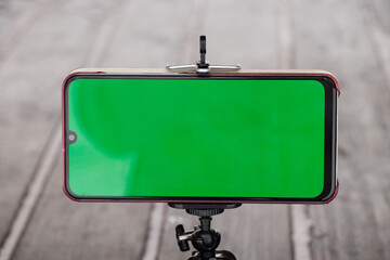 mobile phone with a green screen stands on a flexible stand on the road outside in winter