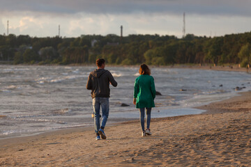 Young couple is walking by the shore of Baltic sea. Windy summer day.