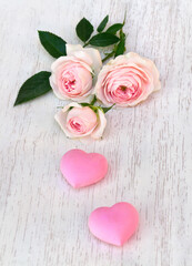 Fototapeta premium Flowers pink roses with pink hearts on background of white painted wooden table with space for text. Decoration of Valentine Day