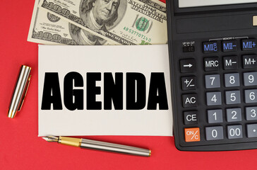 On a red background, among the money, a calculator and a pen lies a sign with the text - AGENDA