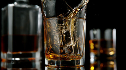 Glass of whisky with splashing liquid and ice rocks inside.