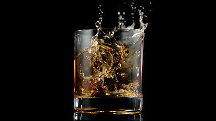 Glass of whisky with splashing liquid and ice rocks inside.