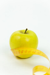 Measuring tape wrapped around a green apple as a symbol of diet. The concept of a healthy lifestyle, food and sports, on a white background. Side view with copy space.