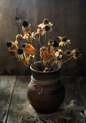 A bouquet of old dried flowers in a vintage jug on a wooden background.