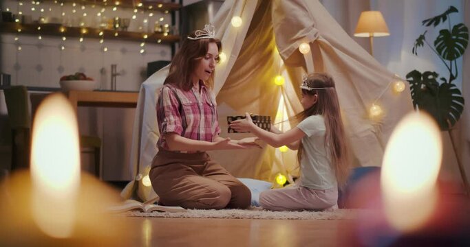 Cute little daughter giving gift box to mother playing together in teepee tent