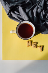 Flat lay composition: cup of tea and biscuits on bright yellow table with gray textile. Morning motivation, breakfast routine, or relaxing break concept. 2021 color trends: yellow and gray. Top view