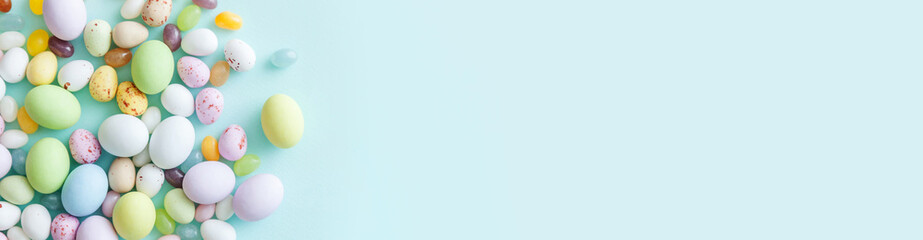 Happy Easter concept. Preparation for holiday. Easter candy chocolate eggs and jellybean sweets isolated on trendy pastel blue background. Simple minimalism flat lay top view copy space. Banner