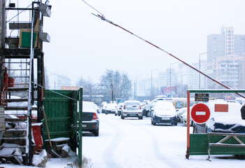 Entering an enclosed private parking lot among the high-rise buildings, no entry sign and a barrier. Many different parked cars covered in snow on a winter day