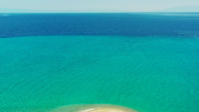Drone fly backwards over Akti Kassandra Halkidiki beach in Greece. The drone starts over the beautiful clear blue sea, and then fly backwards over the sandy beach where there are some people walking