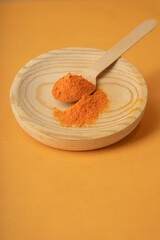 wooden spoon with curcuma on a wooden plate on a plain background