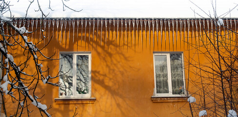 very large icicles hang over two windows on the bright yellow house. freezing rain winter