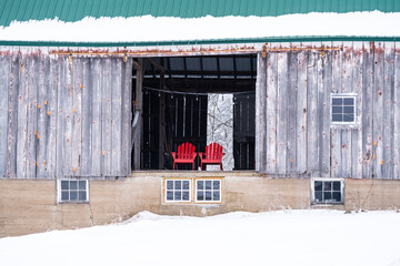 Two red adirondack chairs sitting in a barn door, in winter