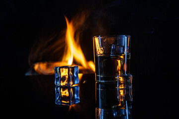 fire ice and glass of whiskey on black background