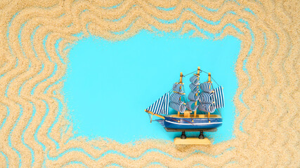 Sand frame with a miniature ship on a blue background. Flat lay. Top view. Copy space. Vacation concept. Travel concept