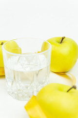 A glass of water and a measuring tape wrapped around three green apples as a symbol of diet. The concept of a healthy lifestyle, food and sports, on a white background. side view