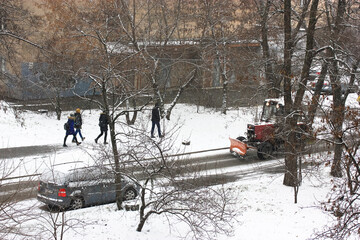 Cleaning city streets from snow in bad weather, snow removal equipment and pedestrians on the sidewalk, view from the window. Kiev, Ukraine, Europe. High quality photo