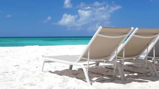 Beach scene with sunbeds close to Caribbean sea with azure water. Tropical island with sunbeds on white sandy shore