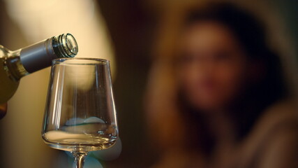 Unknown bartender pouring wine from bottle. Blurred woman taking glass indoors.
